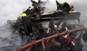 People help rescue workers lift a water hose to extinguish a fire after a plane crashed into a neighbourhood in Ishaga district